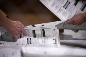 Election worker at polling station with hand-marked paper ballots representing Trump administration requirement for states to phase out electronic voting systems to retain federal funding